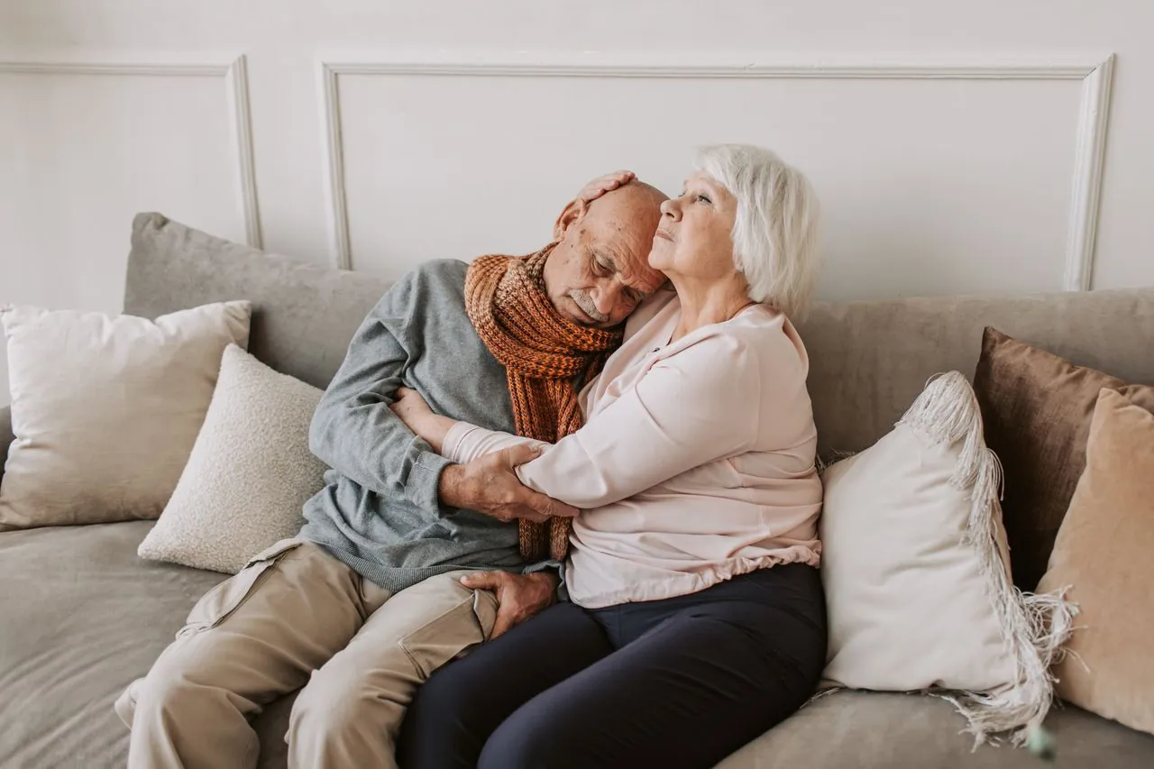 An older woman holding her husband close on the sofa