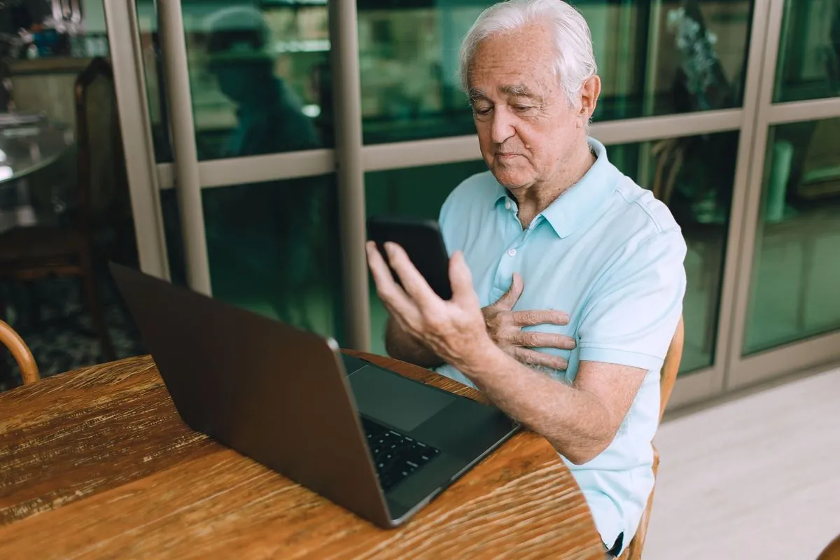 An older man resting a hand on his chest as he follows a breathing exercise on his phone