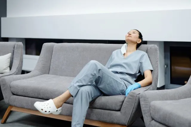 A nurse in scrubs leaning back on a sofa during a break