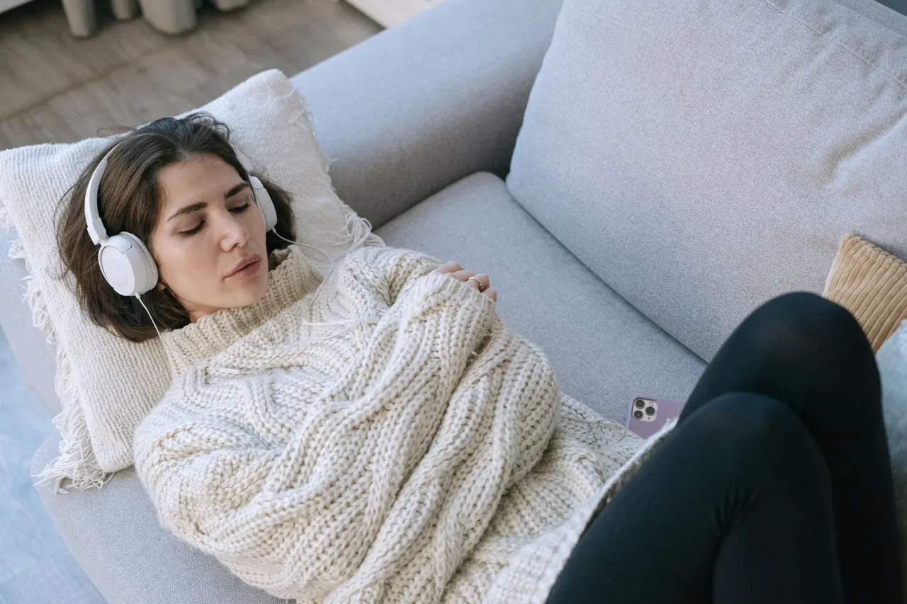 A woman resting on a sofa with headphones on and her eyes closed