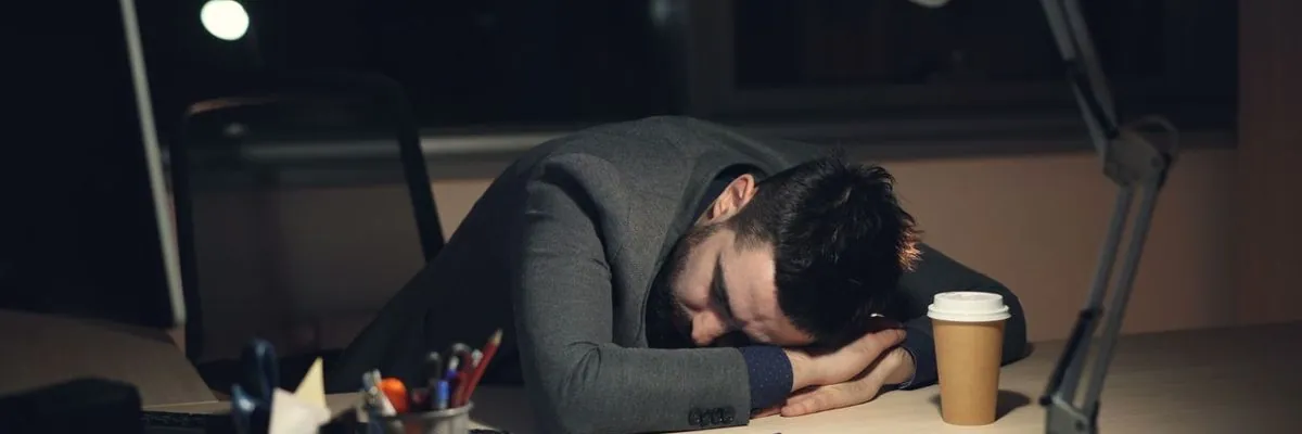 A man asleep at his desk late at night beside a coffee cup