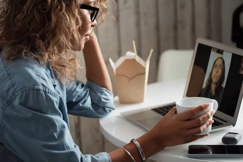 A woman with a cup of tea on a video call with her therapist