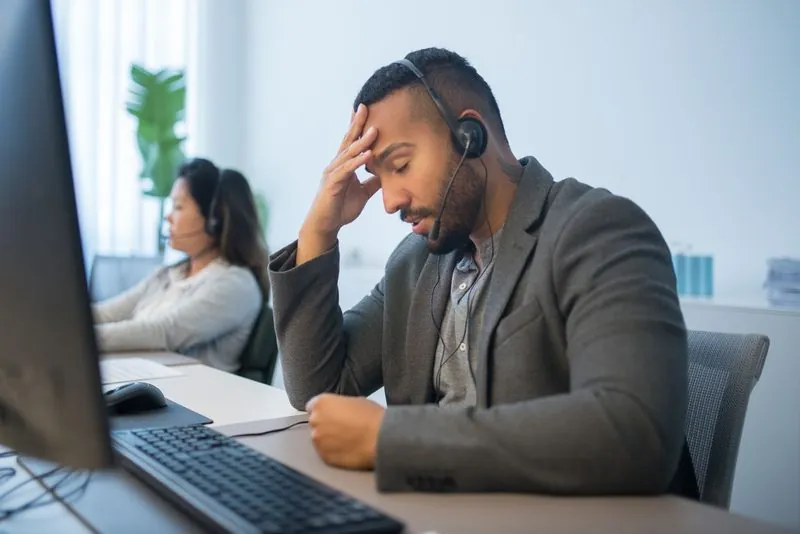 A tired call-centre worker in a headset rubbing his forehead
