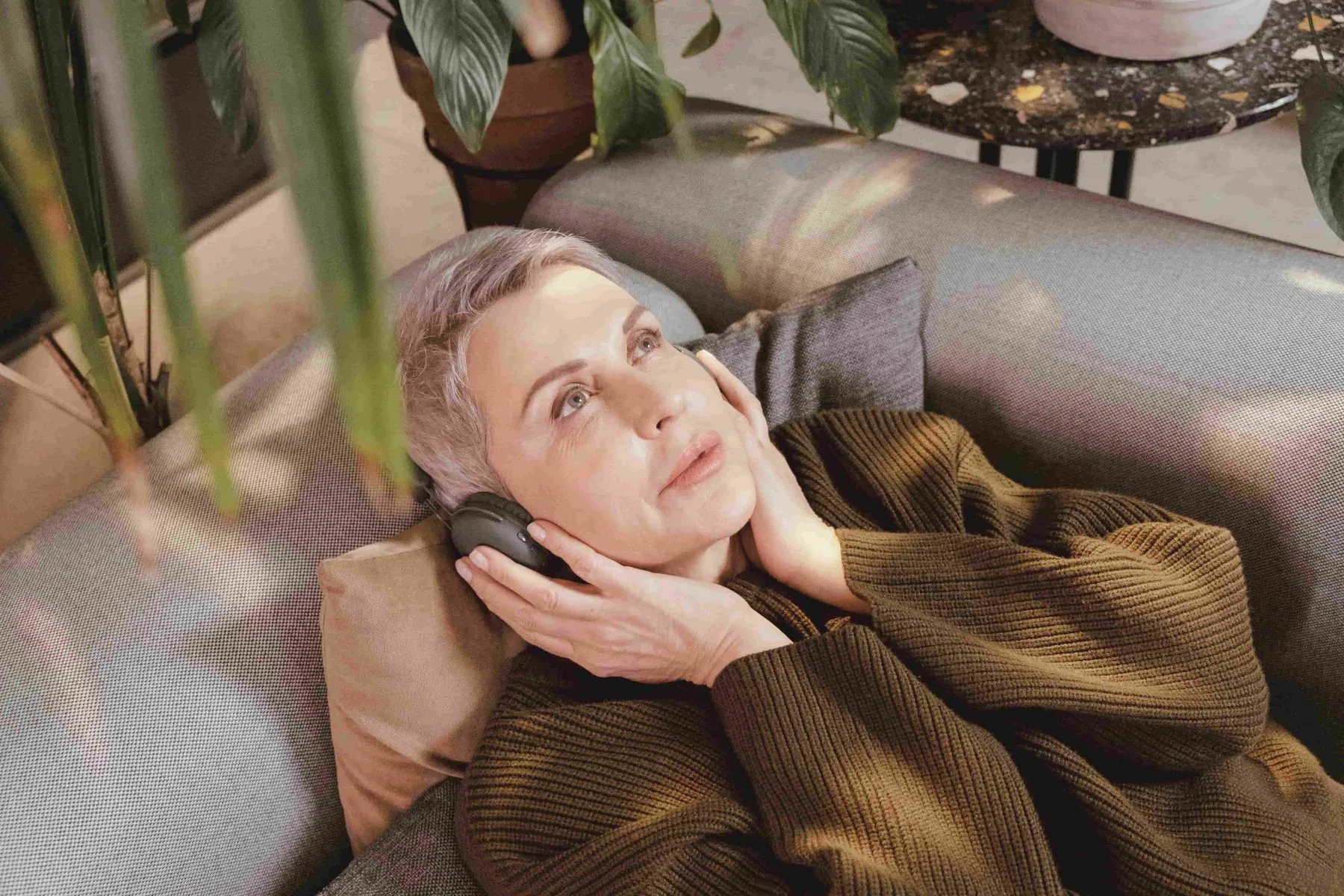 A woman relaxing on a sofa, listening through headphones