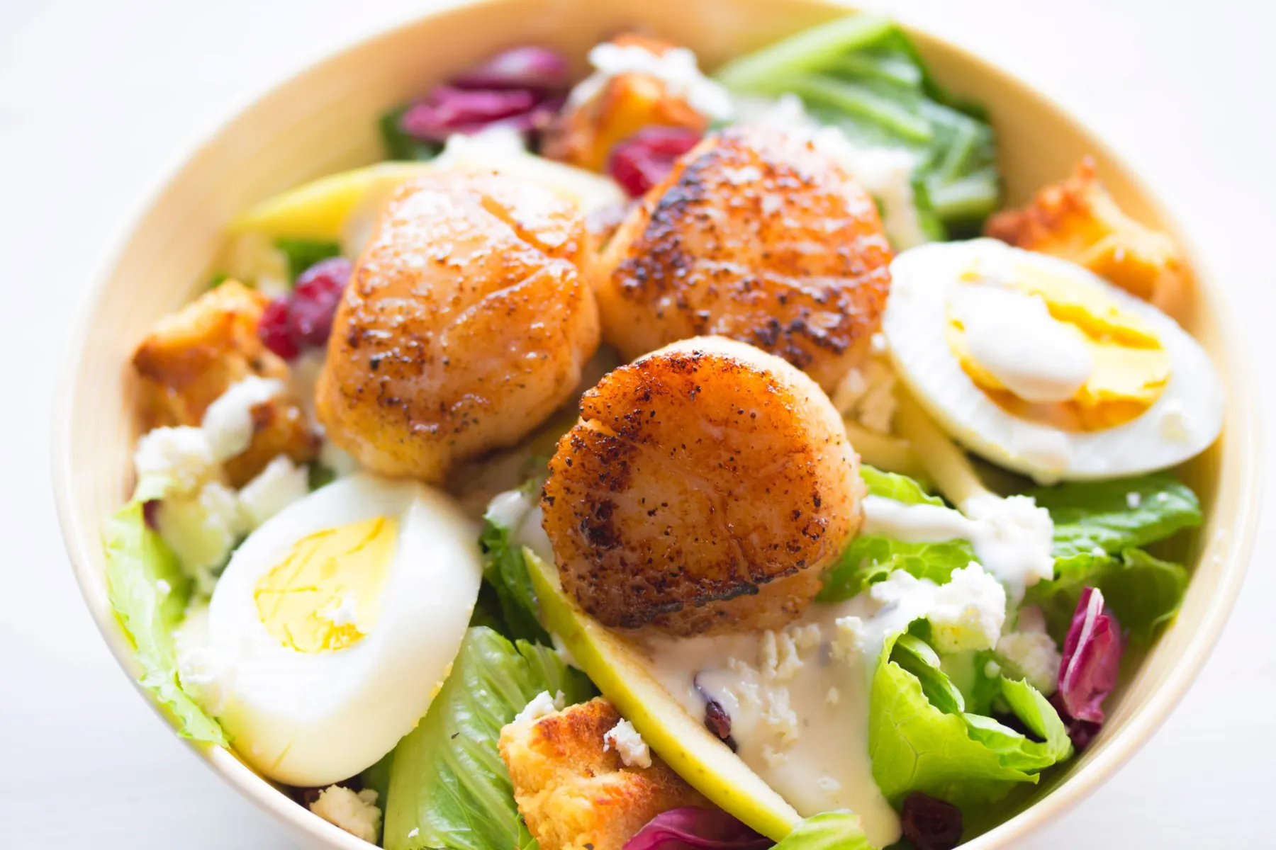 A bowl of seared scallops, boiled eggs and fresh salad