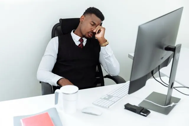 A tired man resting his head in his hand at his office desk