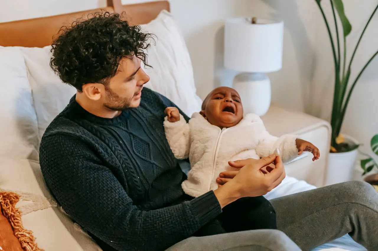 A young dad holding his crying baby on the bed