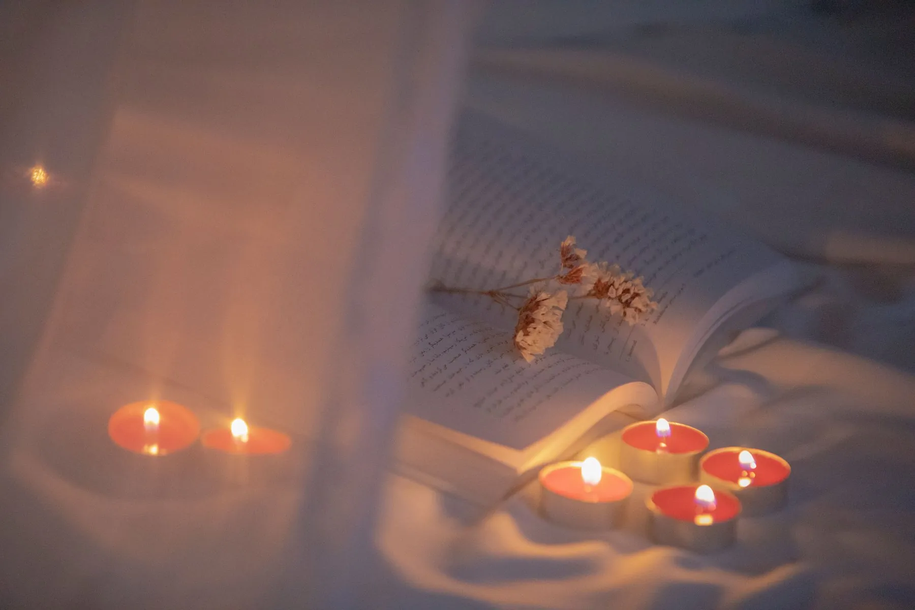 Tea lights glowing beside an open book with dried flowers