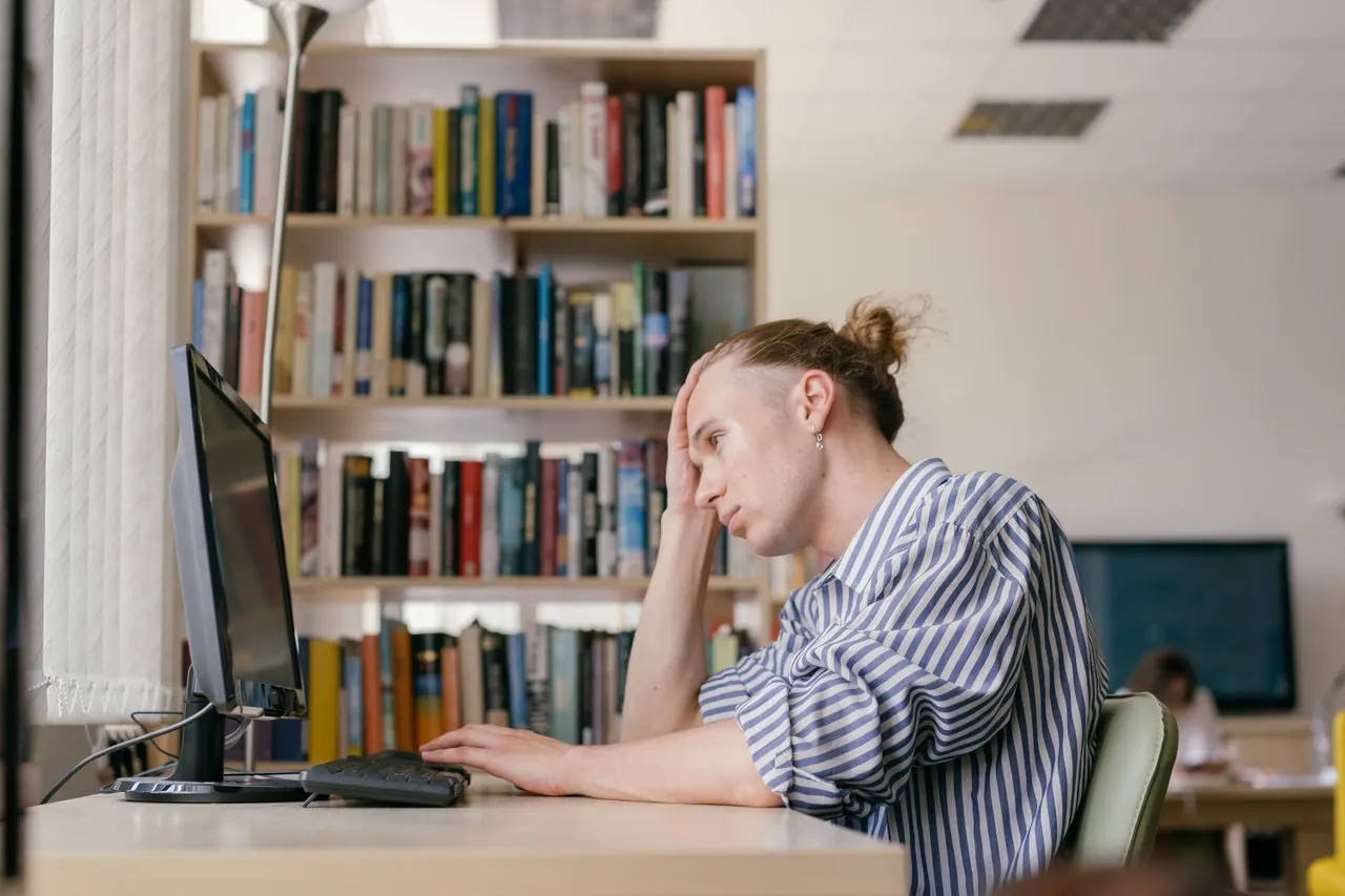 A stressed student resting his head on his hand at a library computer