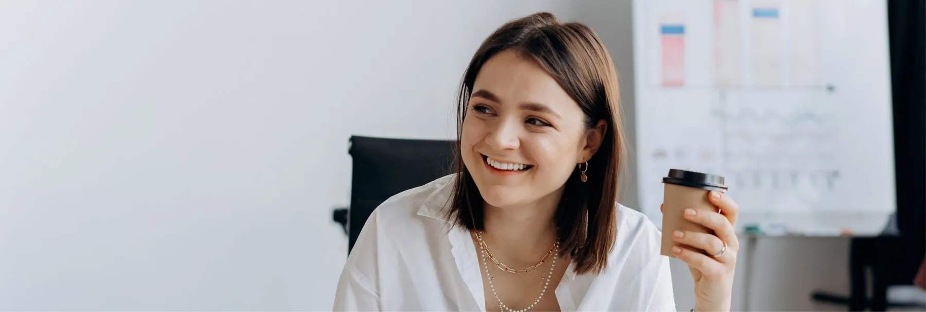 A smiling woman holding a coffee in a bright office