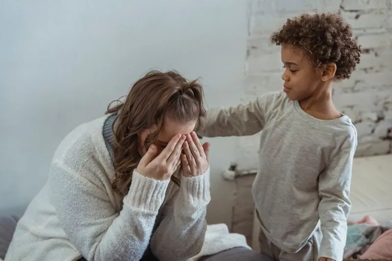 A young child gently comforting his mum, who has her head in her hands
