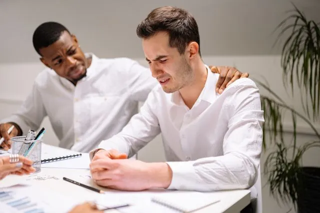 A man comforting a stressed colleague at a desk